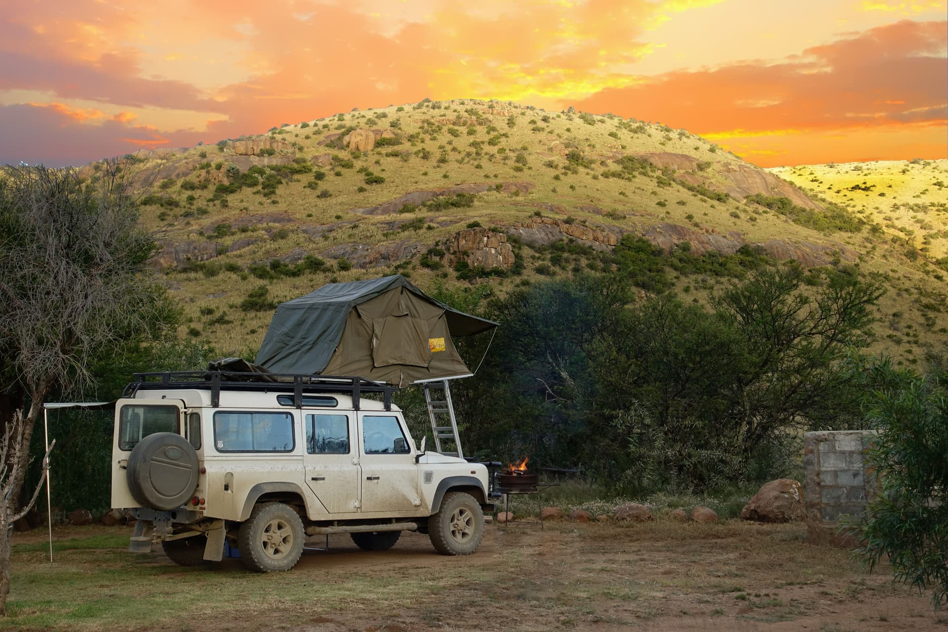 Ein geparktes Reisefahrzeug mit aufgeklapptem Dachzelt und Leiter bei Sonnenuntergang in Bo-Karoo, Südafrika.