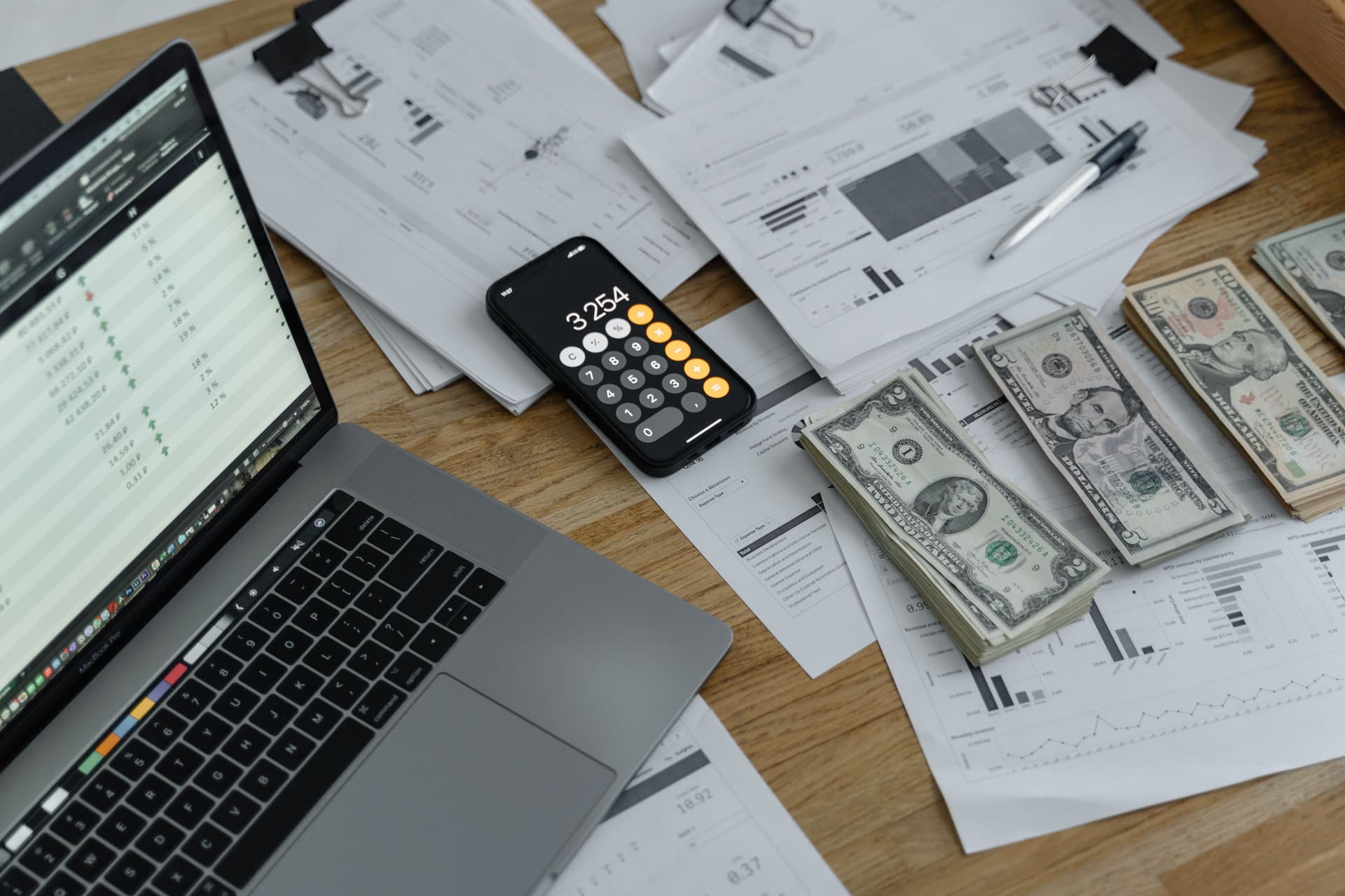 US-Dollar-Noten, Finanzdiagramme, Laptop und ein Smartphone-Taschenrechner auf einem Schreibtisch; illustratives Budgetplanungsfoto.