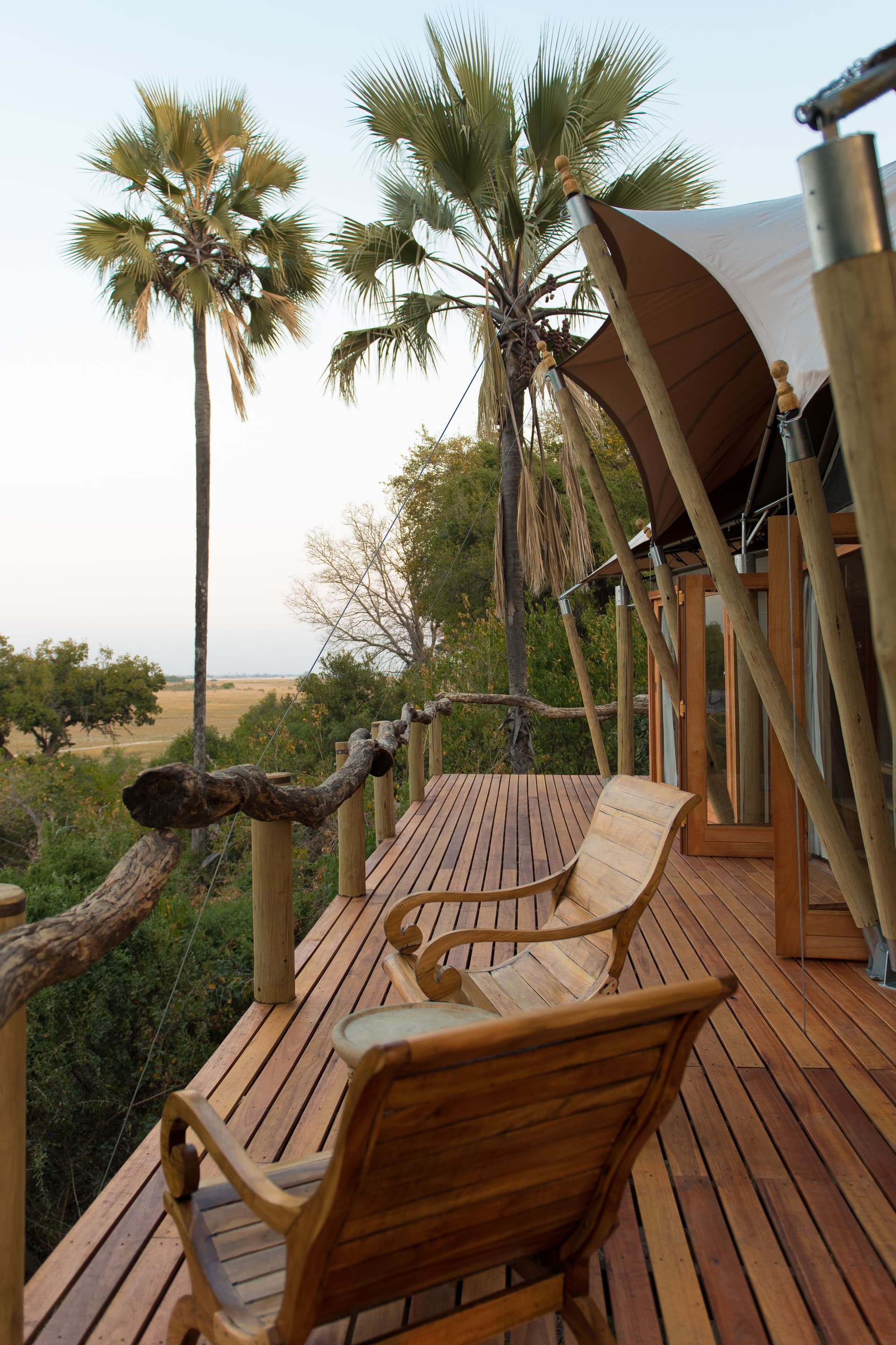 Holzstühle auf der Terrasse einer Zeltlodge zwischen Palmen in Botswana.