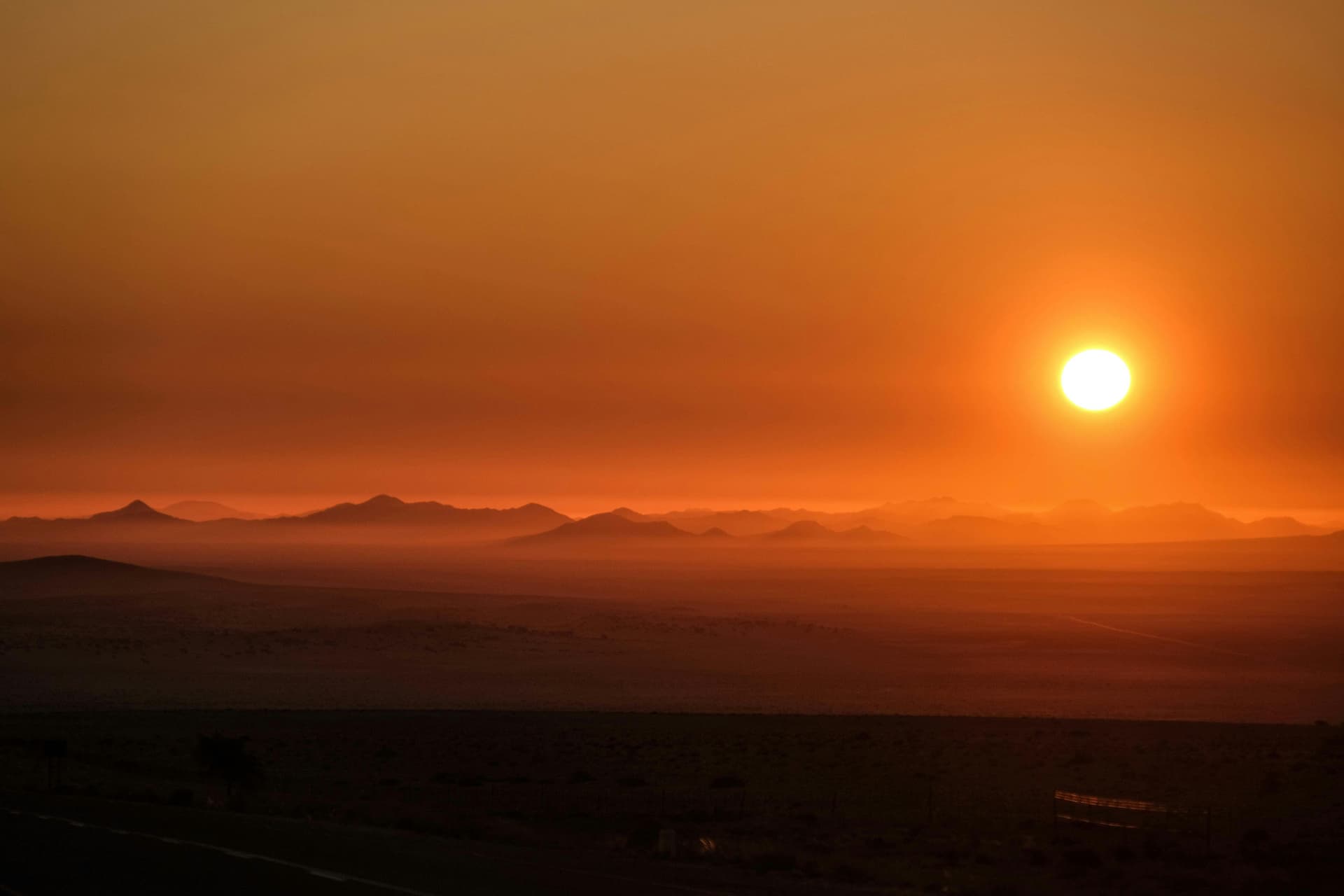 Sonne über entfernten Wüstenbergen in Namibia; illustratives Landschaftsfoto.