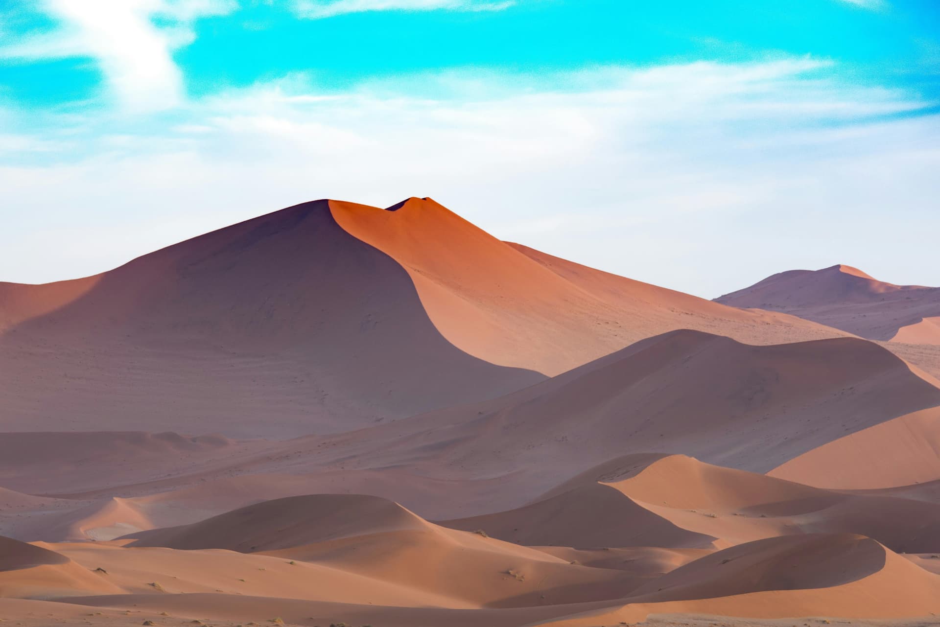 Orangefarbene Sanddünen unter blauem Himmel in Namibia; illustratives Landschaftsfoto.